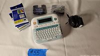 Photo showing Brother label maker, black power adapter, six extra ribbon cartridges, and a lot number on blue tape.
