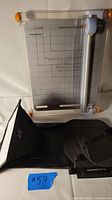 Fiskars paper cutter showing the full base with grid, sliding blade and orange corner grips, along with the black photography accessories below.