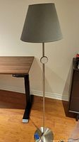 Floor lamp positioned next to a desk and cabinet, showing full lamp with gray shade and metal base and stand.