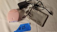Pink FOREO Luna facial cleansing device with charger and storage pouch laid out on a light-colored fabric surface.