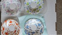 Top view of the four bone china saucers showing distinct seasonal floral patterns in pink/purple, blue/green, orange/brown, and blue/gray.