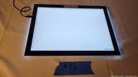 Top view of the Huion LED light pad powered on, glowing white surface with ruler markings along the edges and Huion logo on bottom right corner.