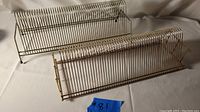 Two mid-century modern vintage metal record album holders showing horizontal rows of parallel metal wires with legs for standing on surfaces.