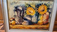Framed oil painting featuring two sunflowers in blue vase along with pottery and lemons on a table, with warm yellow and brown tones.