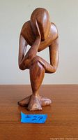 Front view of wooden abstract statue of pondering person, showing full figure and wood texture.