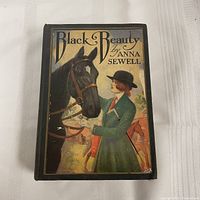Front cover of the 1927 edition of Black Beauty by Anna Sewell showcasing a colored illustration of a woman and a horse.