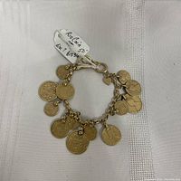 Bracelet laid flat showing all attached coin-shaped charms and the clasp with heart charm.