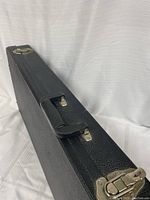 Closed black hard case for electric bass guitar with metal latches and carrying handle, showing slight wear.