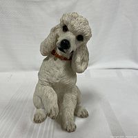 Front view of handcrafted white poodle figurine with textured fur, brown collar, sitting position with one paw raised.