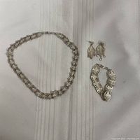 Complete set of silver-tone jewelry placed on white fabric: necklace, bracelet, earrings.