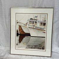 Framed art showing two wooden boats named 'Miss Nikko' and 'SPL' docked with reflections in water.