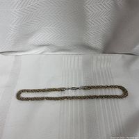 Full length view of rope chain necklace laid flat on fabric background, showing chain pattern and clasp.