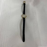 Full view of the watch laid out showing the black leather strap and gold-tone case on a white background.