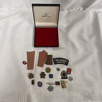 Top view of all vintage Girl Guides pins, patches, and uniform fabric pieces arranged on white cloth with Zenith box lid opened above.