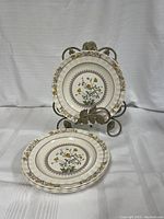 Four vintage Spode plates stacked and one displayed on decorative metal stand showing floral pattern and scalloped edges