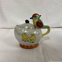 Front side view showing woodpecker handle, lid with black knob, and chick illustration.