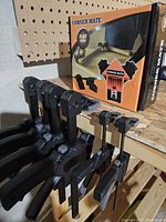 Various bar clamps and 4 boxed corner clamps stored on a wooden shelf.