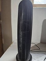 Front view of black vertical tower air purifier showing grille and base.