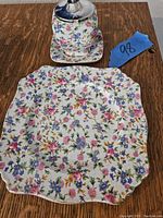 Jam jar with floral patterns and metal lid on a matching small square plate with floral patterns, shown on wooden surface with blue lot number tag.