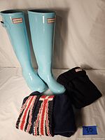 Photo of turquoise Hunter tall rain boots with one pair of solid black fleece liners and one pair of navy blue fleece liners with red, white, and black knit cuffs.