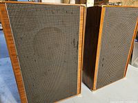Pair of vintage Grundig 731 speakers showing front grille cloth and walnut wood veneer sides, one speaker cosmetically better than the other.
