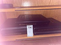 Black binders on wooden shelf with label showing lot number 138 and brief note '22kt Baseball Cards 1998 World Series'