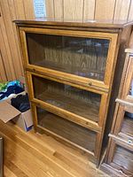 Front view of wooden barrister bookcase with three glass-fronted sections, each door with a knob.
