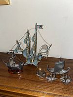 Photo showing all six metal boat sculptures arranged on a wooden surface.