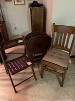 Three pieces of furniture including folding wooden slat chair, oak caned seat chair with cushion, and a set of folding TV tray tables with stand