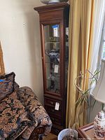 Full view of the dark wood framed display cabinet with glass front door and visible contents on glass shelves inside.