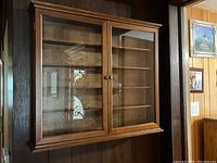 Full front view of the wood framed display case mounted on dark wood-paneled wall showing two glass doors and interior shelves.