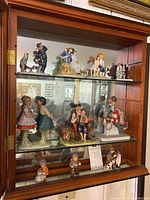 Wide shot of all 10 Norman Rockwell figurines displayed in glass cabinet, showing various scenes including children and adults in retro style.