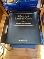 Photo of the closed black binder with gold embossed text: '22kt Gold Baseball Cards Authorized by Major League Baseball Jerry Bieber, M.D.'