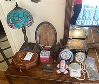 Wide shot of all items on wooden dresser including Tiffany style lamp, mirror, clocks, boxes, and other small items.