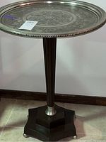 Full view of the table showing round metal top with embossed pattern and cylindrical pedestal.