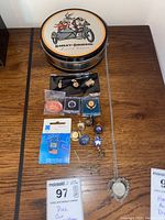 Overall view of lot showing Harley-Davidson canister, various pins, coin necklace, and tie clips arranged on table