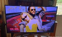 Front view of Samsung TV powered on displaying a colorful image showing people with sunglasses. Shows the screen condition and display quality.