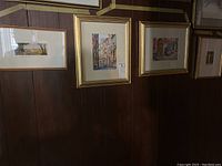 Four framed pieces hanging on a dark wood paneled wall, showing Jerusalem-inspired street and cityscape scenes in gold and wood-toned frames