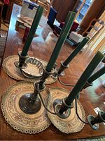 Full view of the three-arm weighted silver candelabra with green candles on a wooden table with placemats.
