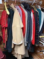 Photo showing various women's sweaters and coats hanging on a clothing rack including a red patterned scarf, black and beige coats, and other garments