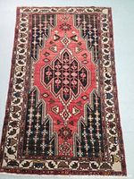 Full view of Persian Mazlegan rug showing geometric and tribal designs in red, black, and cream.