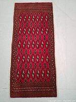 Full view of the rectangular hand knotted Turkmen wool rug showing red field and geometric motifs.