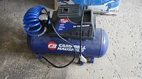 Front view of Campbell Hausfeld air compressor with blue coil hose and power cord lying on ground.