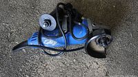 Blue electric angle grinder with grinding disc attached and power cord in visible condition.