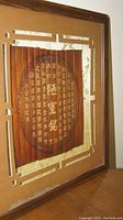 Diagonal angled close-up photo of the framed bamboo art featuring Chinese calligraphy and partial view of the frame and matting corner.