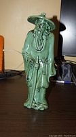 Front view of green glazed ceramic figure statue of elderly Asian man in robe and conical hat.