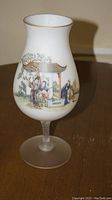Full view of the glass cup showing the shape, white glass body with painted scene, and transparent base.