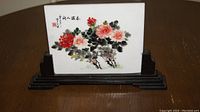 Hand painted Asian floral art on ceramic tile shown in wooden display stand, showing full piece.