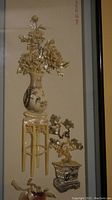 Complete view of shadow box showing three-dimensional shell art floral vase on a stand and potted pine tree