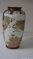 Side view of tall ceramic vase showing floral and geometric patterns with gold accents on brown and white background.